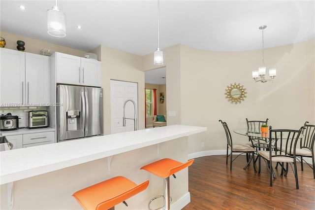 kitchen featuring stainless steel fridge, dark hardwood / wood-style flooring, decorative light fixtures, and a kitchen breakfast bar