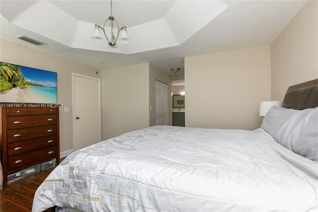 bedroom featuring a tray ceiling, dark wood-type flooring, and an inviting chandelier