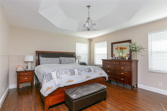 bedroom with dark hardwood / wood-style floors, a tray ceiling, and a notable chandelier