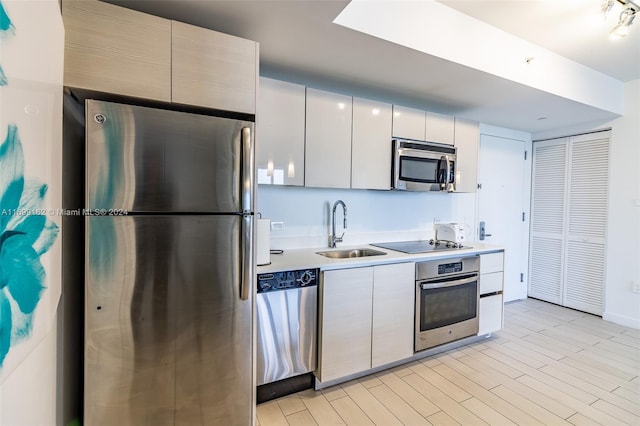 kitchen with white cabinetry, sink, stainless steel appliances, and light hardwood / wood-style floors