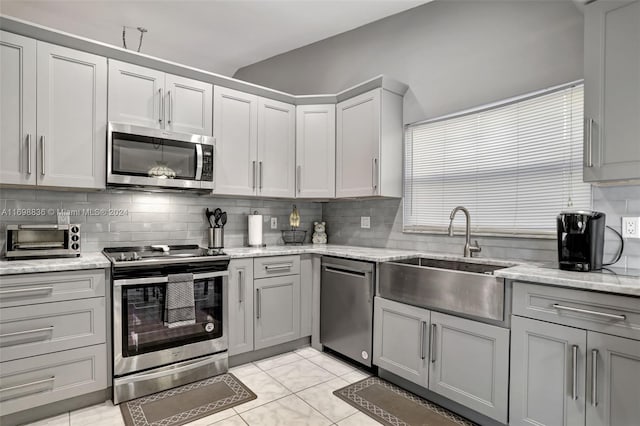 kitchen featuring light stone countertops, sink, stainless steel appliances, decorative backsplash, and light tile patterned floors