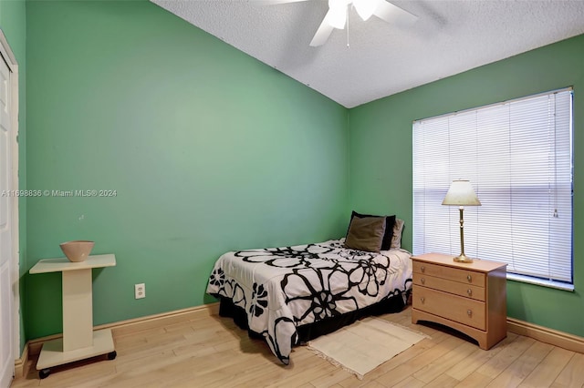 bedroom with vaulted ceiling, ceiling fan, light hardwood / wood-style flooring, and a textured ceiling