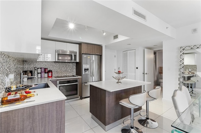 kitchen with white cabinetry, stainless steel appliances, a kitchen island, backsplash, and a kitchen bar