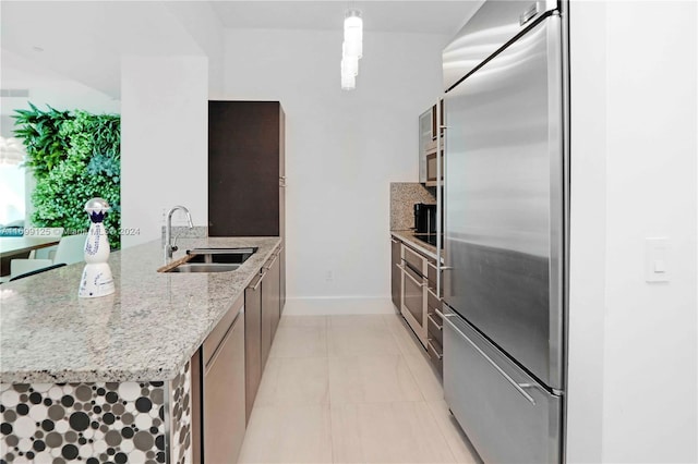 kitchen with kitchen peninsula, light stone counters, stainless steel appliances, sink, and pendant lighting