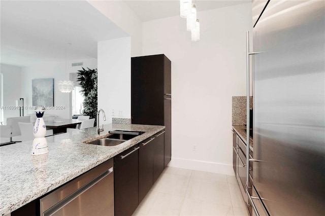 kitchen with light stone counters, stainless steel appliances, sink, pendant lighting, and light tile patterned floors