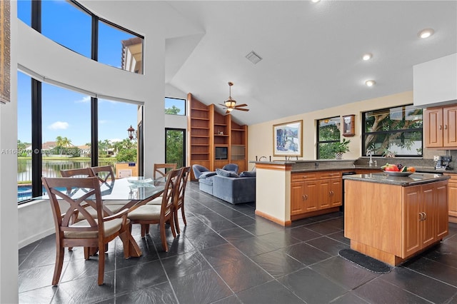 kitchen with ceiling fan, a kitchen island, high vaulted ceiling, kitchen peninsula, and a water view