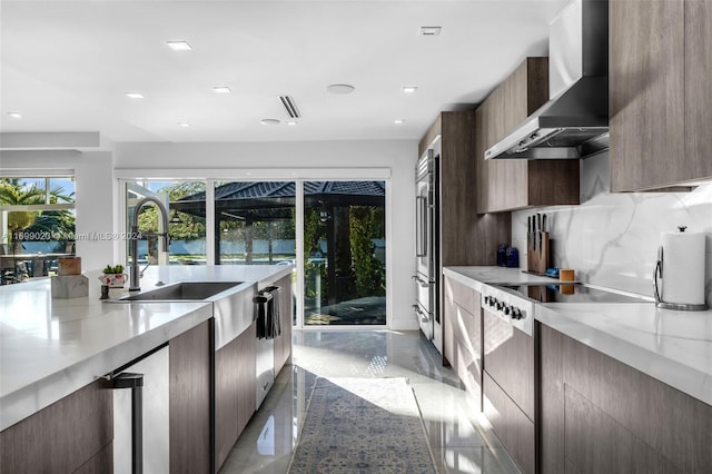 kitchen featuring backsplash, wall chimney range hood, sink, light stone countertops, and appliances with stainless steel finishes