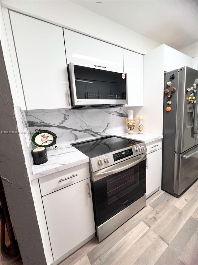 kitchen with backsplash, light hardwood / wood-style flooring, white cabinets, and stainless steel appliances