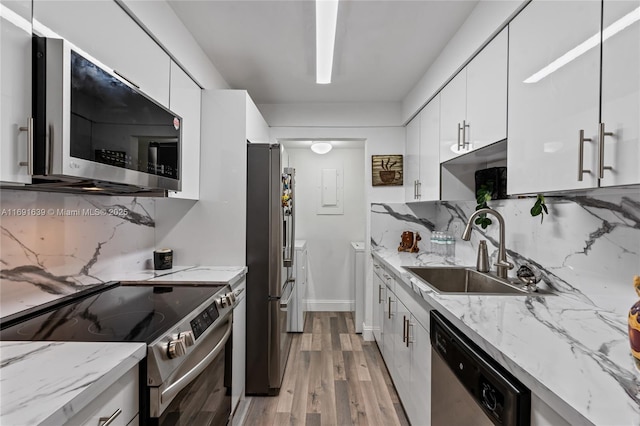 kitchen featuring sink, white cabinetry, stainless steel appliances, light hardwood / wood-style floors, and decorative backsplash