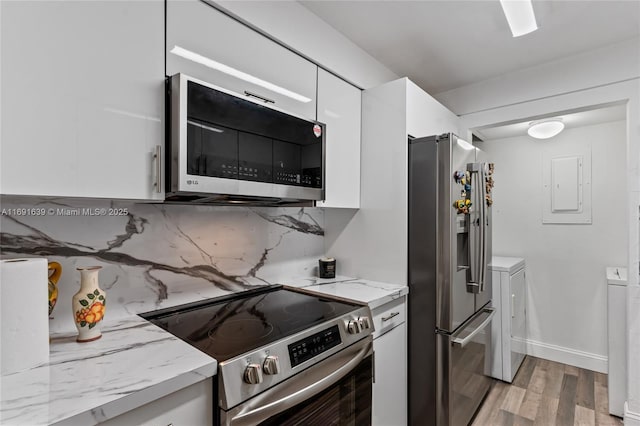 kitchen featuring appliances with stainless steel finishes, white cabinets, decorative backsplash, light hardwood / wood-style floors, and washing machine and dryer