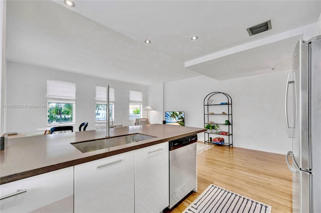 kitchen with white cabinets, sink, stainless steel appliances, and light hardwood / wood-style floors