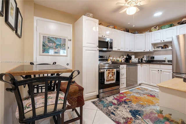 kitchen with appliances with stainless steel finishes, ceiling fan, sink, light tile patterned floors, and white cabinets