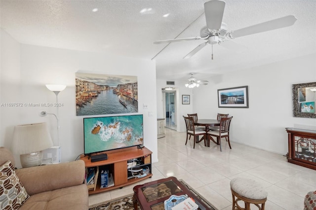 living room featuring ceiling fan, light tile patterned floors, and a textured ceiling