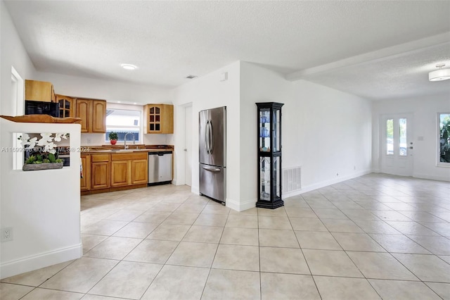 kitchen featuring appliances with stainless steel finishes, a textured ceiling, light tile patterned floors, and beam ceiling