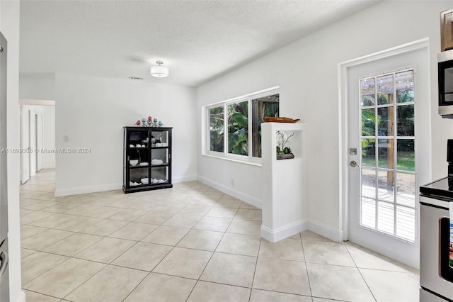 doorway featuring plenty of natural light, light tile patterned flooring, and a textured ceiling