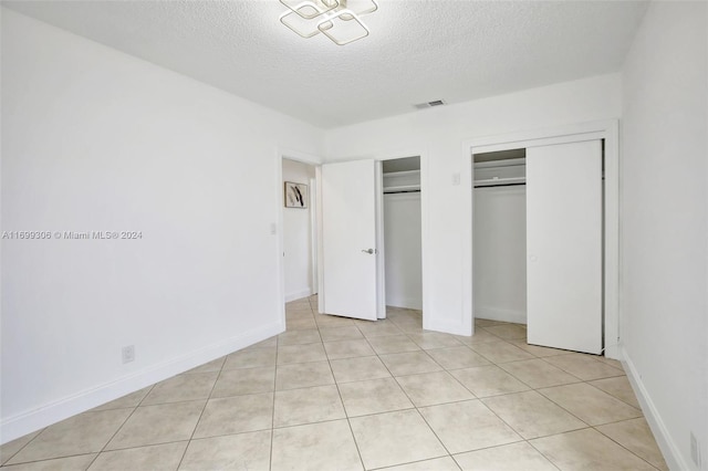 unfurnished bedroom featuring a textured ceiling, two closets, and light tile patterned flooring