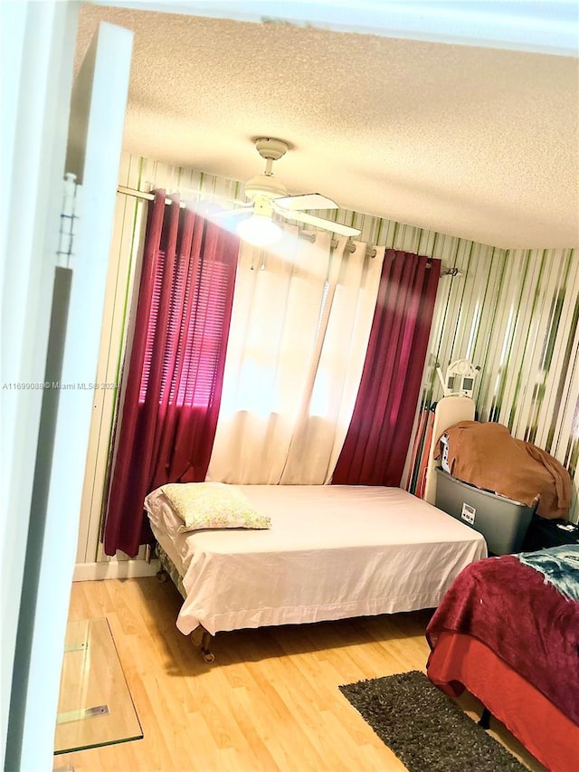 bedroom with ceiling fan, wood-type flooring, and a textured ceiling