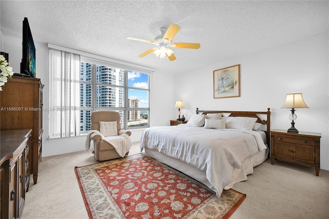 bedroom with ceiling fan, light colored carpet, and a textured ceiling