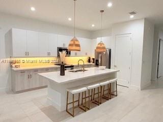 kitchen with white cabinets, sink, hanging light fixtures, an island with sink, and stainless steel appliances