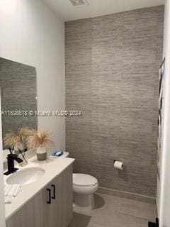 bathroom featuring tile patterned floors, vanity, toilet, and tile walls