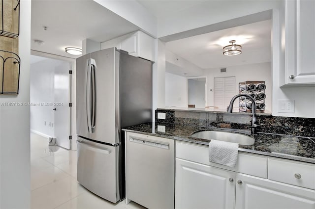 kitchen with dishwasher, dark stone counters, sink, white cabinetry, and stainless steel refrigerator