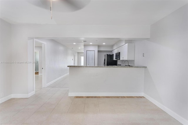 3241 NE 17th Ave, Oakland Park, FL 33334 - kitchen with black microwave, freestanding refrigerator, white cabinets, light stone counters, and a peninsula