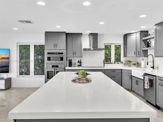 kitchen with gray cabinetry, stainless steel appliances, sink, wall chimney range hood, and a center island