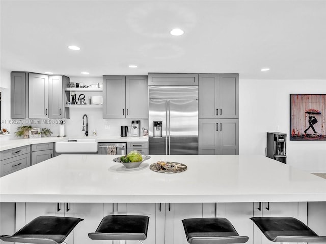 kitchen featuring a kitchen bar, stainless steel appliances, gray cabinets, and sink