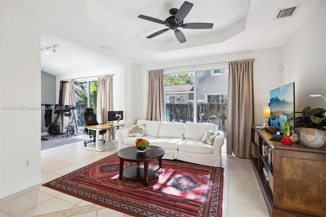 tiled living room featuring a raised ceiling, a healthy amount of sunlight, track lighting, and ceiling fan