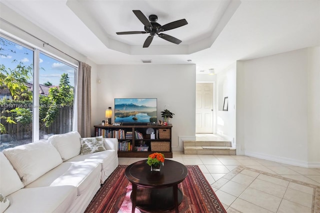 living room with ceiling fan, a tray ceiling, and light tile patterned floors