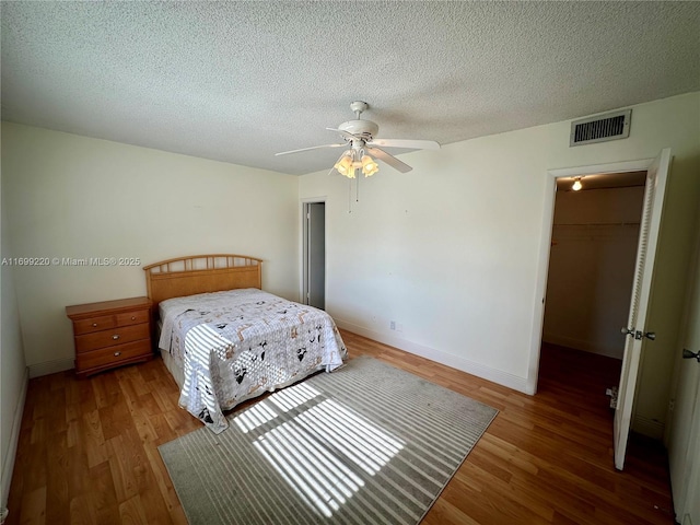 bedroom featuring ceiling fan, hardwood / wood-style floors, a textured ceiling, a walk in closet, and a closet