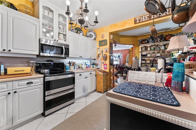 kitchen with white cabinets, light tile patterned floors, appliances with stainless steel finishes, decorative light fixtures, and a chandelier