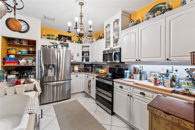 kitchen with hanging light fixtures, stainless steel appliances, light tile patterned floors, an inviting chandelier, and white cabinets