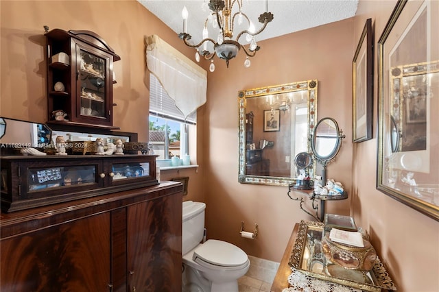 bathroom featuring toilet, tile patterned flooring, a textured ceiling, and an inviting chandelier