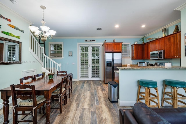 kitchen with appliances with stainless steel finishes, light stone counters, ornamental molding, dark wood-type flooring, and an inviting chandelier