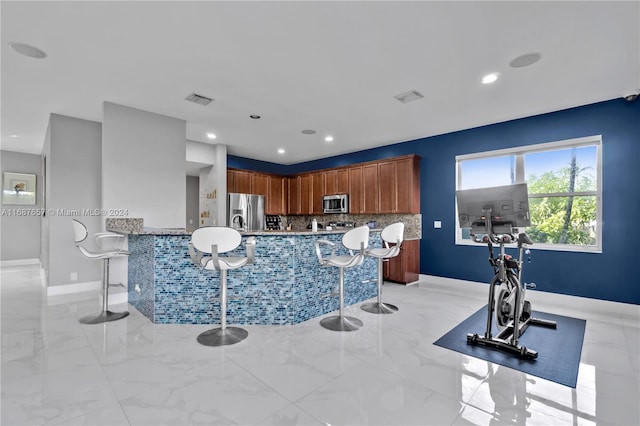 kitchen with a kitchen bar, stainless steel appliances, kitchen peninsula, and tasteful backsplash