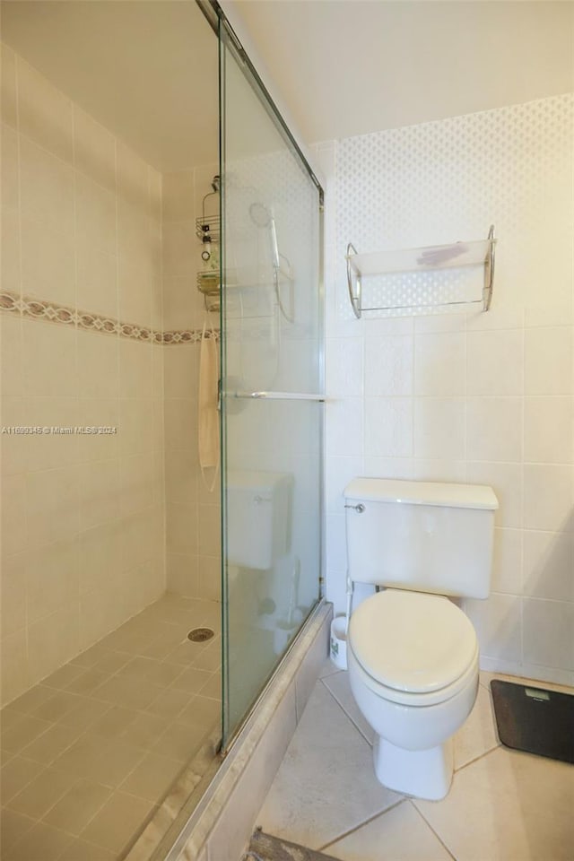 bathroom with tile patterned flooring, toilet, tile walls, and a shower with shower door