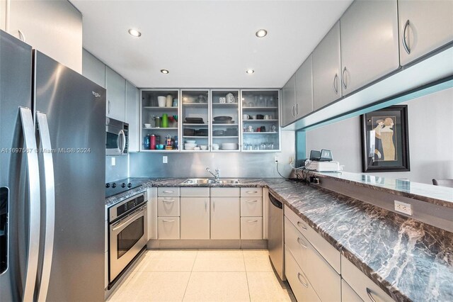 kitchen with gray cabinetry, sink, stainless steel appliances, dark stone counters, and light tile patterned floors