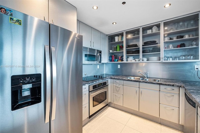 kitchen featuring dark stone countertops, sink, light tile patterned floors, and stainless steel appliances