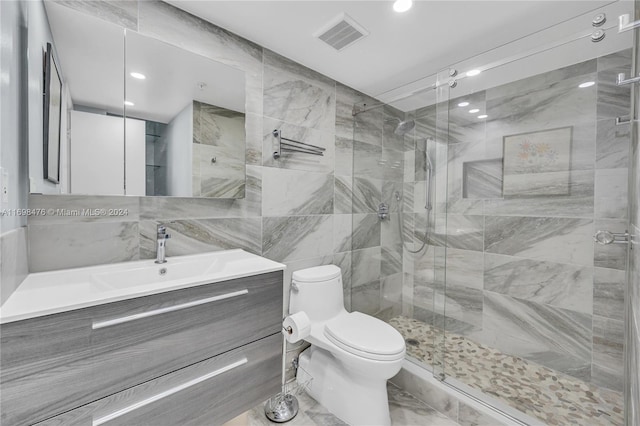 bathroom with vanity, toilet, a shower with shower door, and tile walls