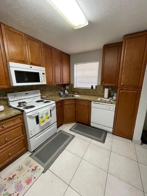 kitchen featuring a textured ceiling, decorative backsplash, light tile patterned floors, and white appliances