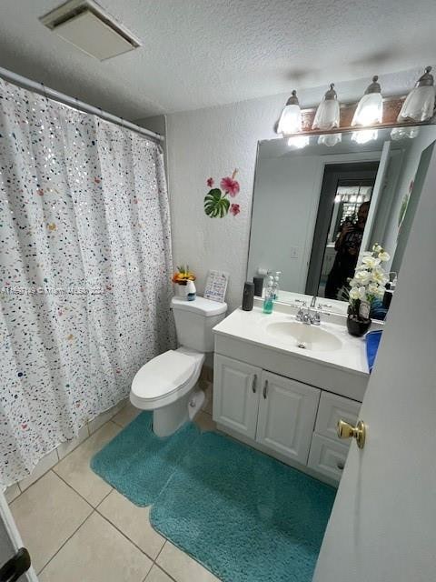 bathroom featuring tile patterned flooring, vanity, a textured ceiling, and toilet