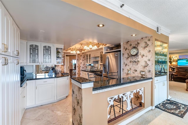 kitchen with stainless steel fridge, dark stone countertops, a textured ceiling, white cabinets, and kitchen peninsula