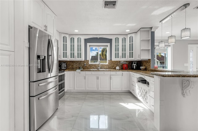 kitchen featuring pendant lighting, decorative backsplash, dark stone countertops, appliances with stainless steel finishes, and white cabinetry