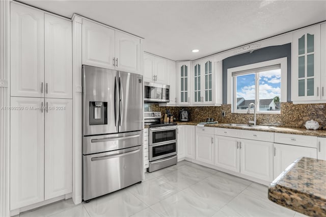 kitchen with appliances with stainless steel finishes, backsplash, sink, stone countertops, and white cabinets