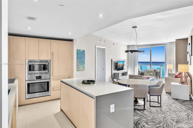 kitchen with light brown cabinets, a kitchen island, pendant lighting, and appliances with stainless steel finishes