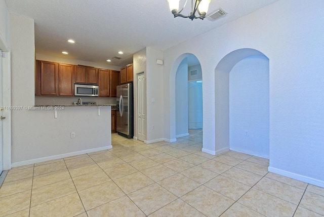 kitchen with appliances with stainless steel finishes, light tile patterned flooring, a kitchen bar, kitchen peninsula, and a chandelier