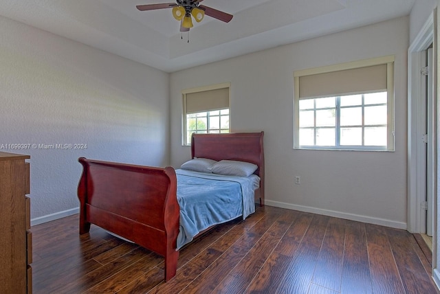 bedroom with a raised ceiling, ceiling fan, and dark wood-type flooring