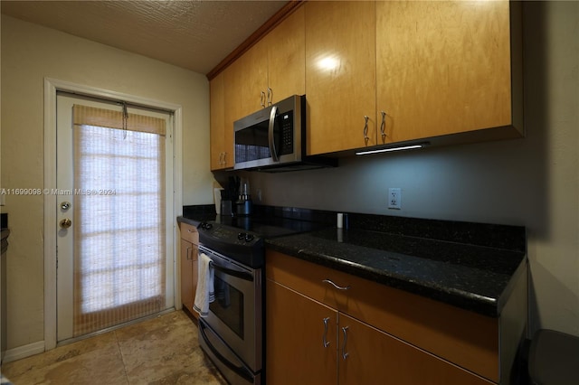 kitchen with a textured ceiling, appliances with stainless steel finishes, and dark stone counters