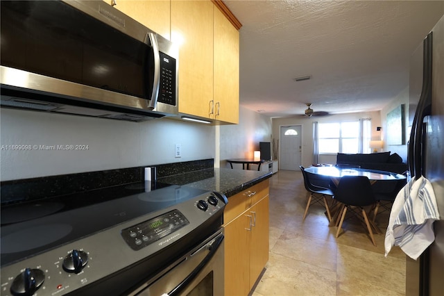 kitchen featuring ceiling fan, stainless steel appliances, dark stone countertops, a textured ceiling, and light brown cabinetry